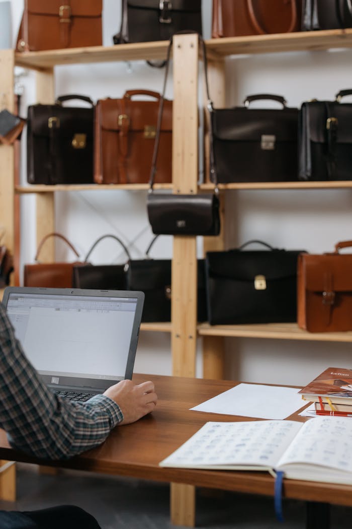 Businessman working on laptop in leather shop with briefcases on shelves.